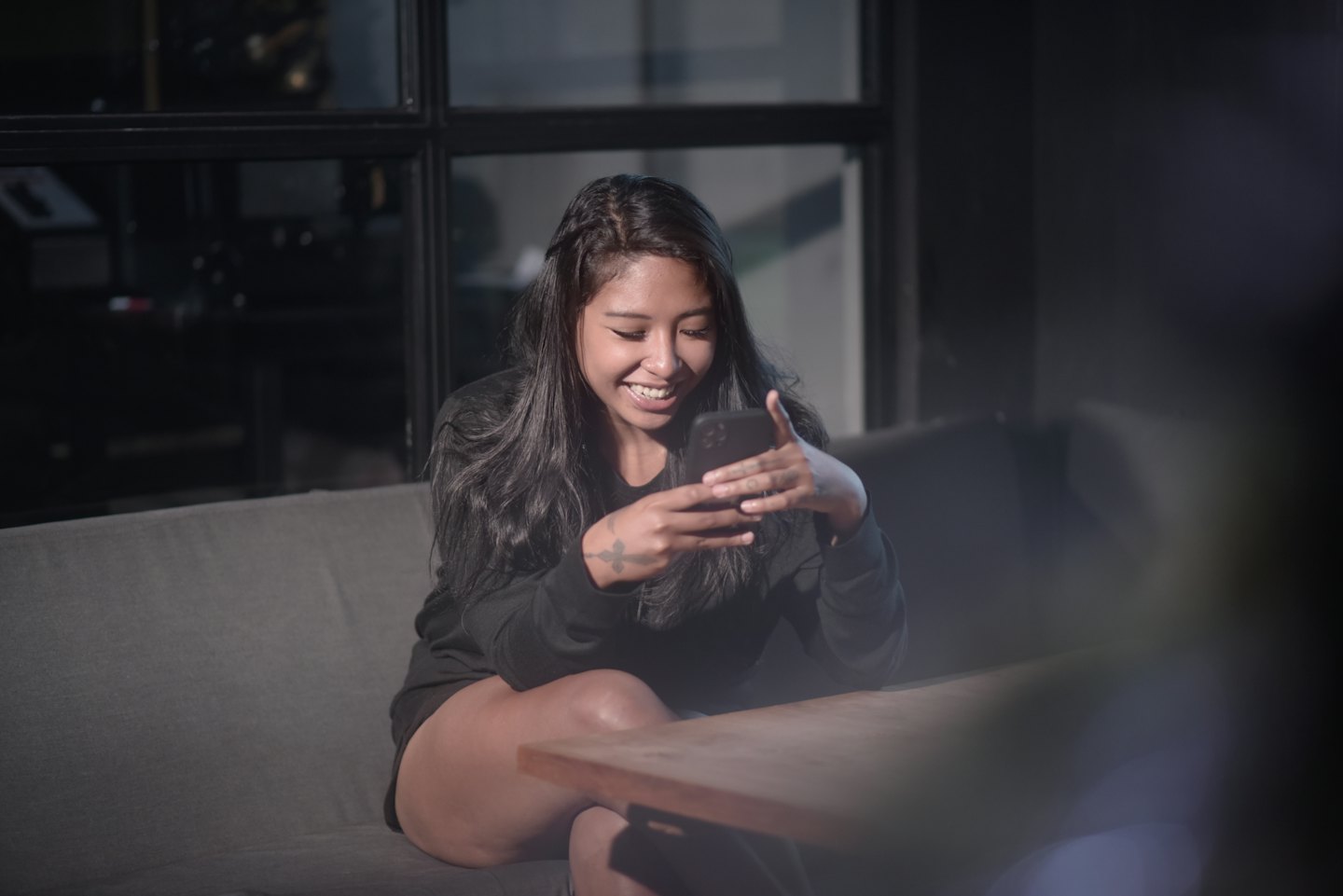 Una donna sorride guardando il suo smartphone su un divano.